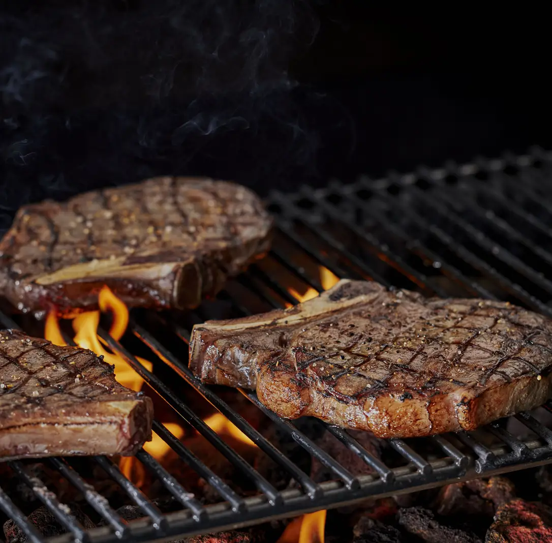 Grilled steaks sizzling over an open flame on a barbecue grill.