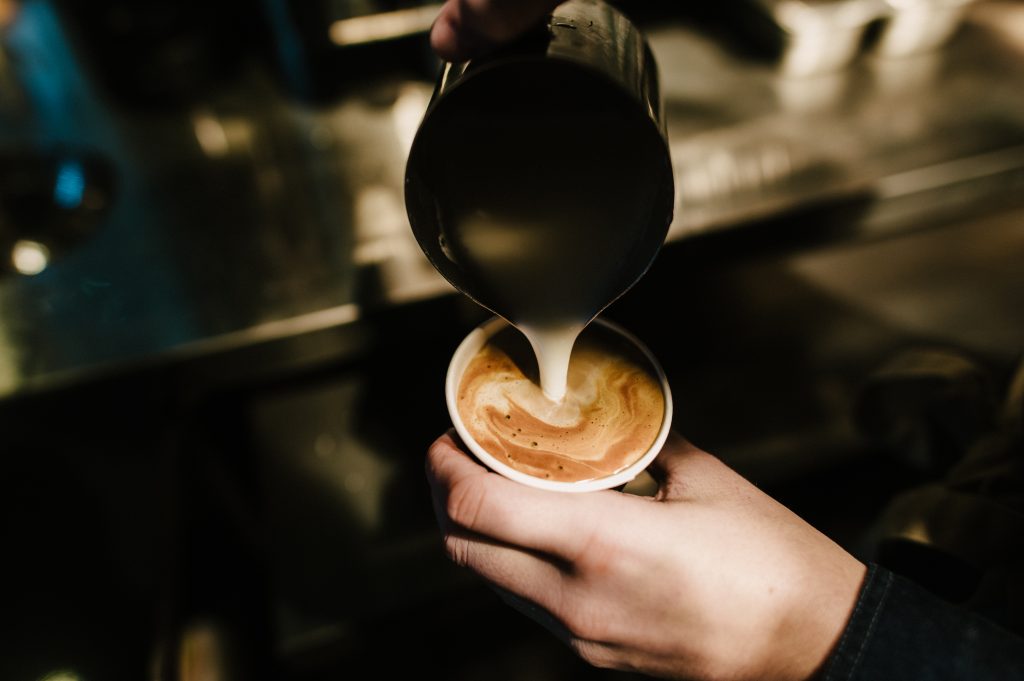 Barista pouring milk into a coffee cup, creating a latte art design.