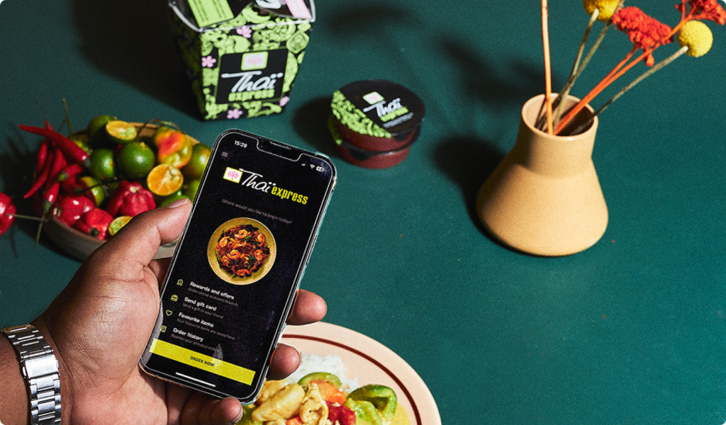 Hand holding a phone displaying Thai Express menu with fresh ingredients and decor.