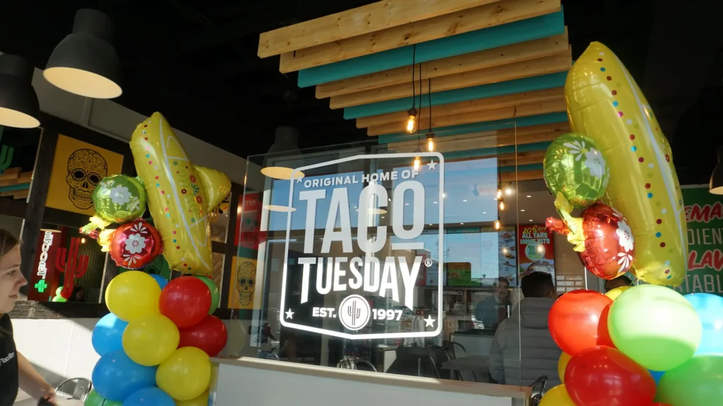 TacoTime interior featuring the "Original Home of Taco Tuesday Est. 1997" sign with colorful chili pepper balloons and festive decor.