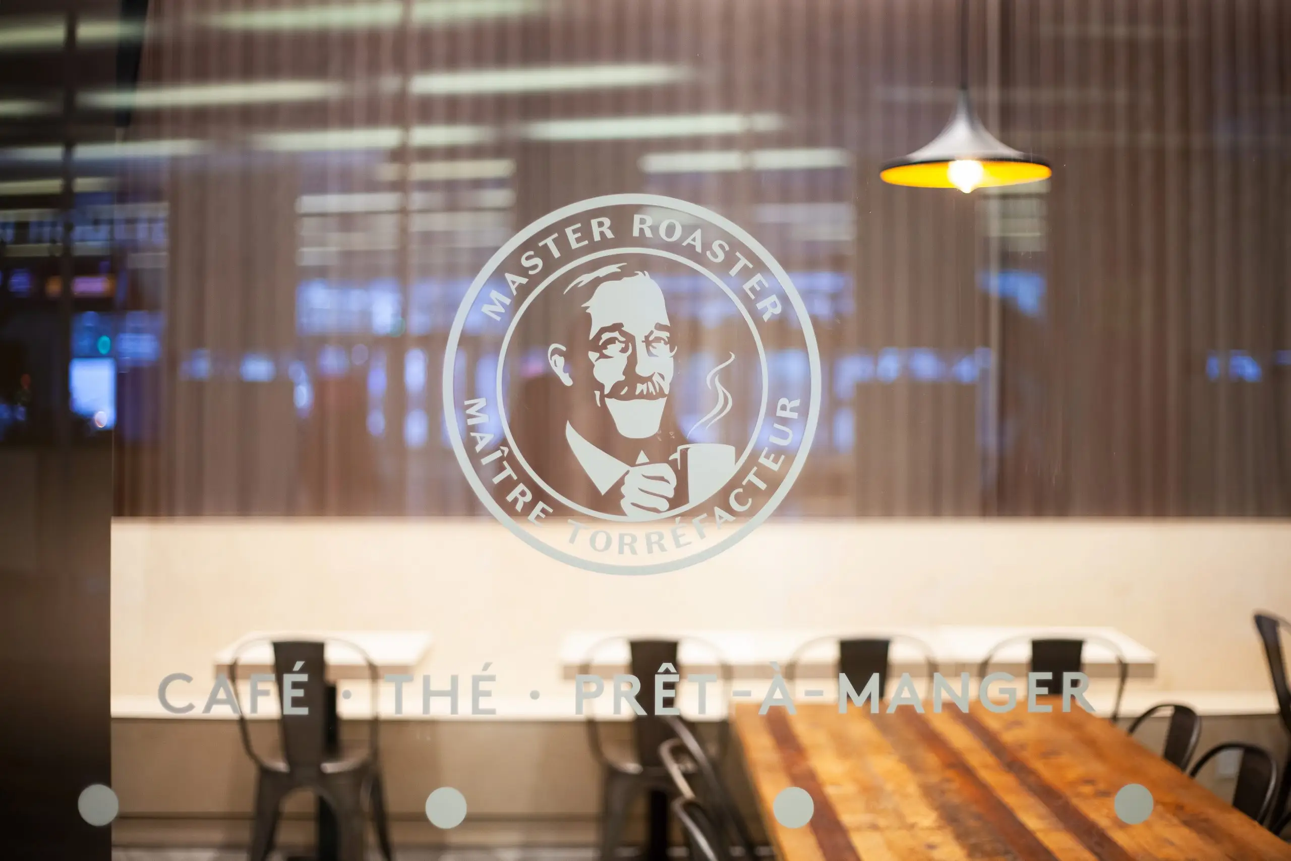 Master Roaster logo on café window with wooden dining table in background.